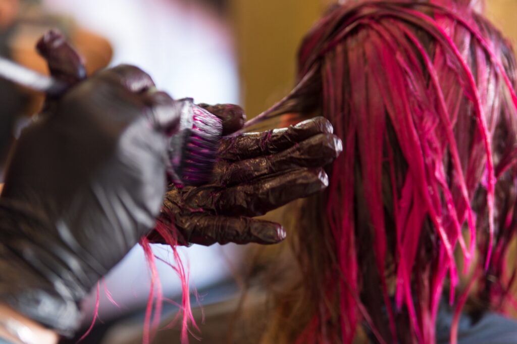 Hair dresser dying a woman's blond hair pink.